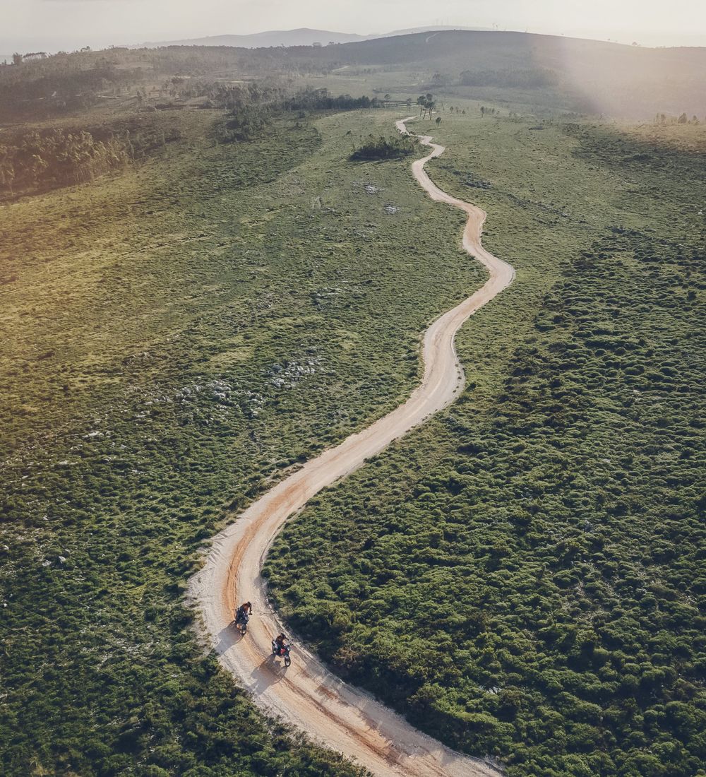 Aerial view of two motorcycles on a winding dirt road through green hills