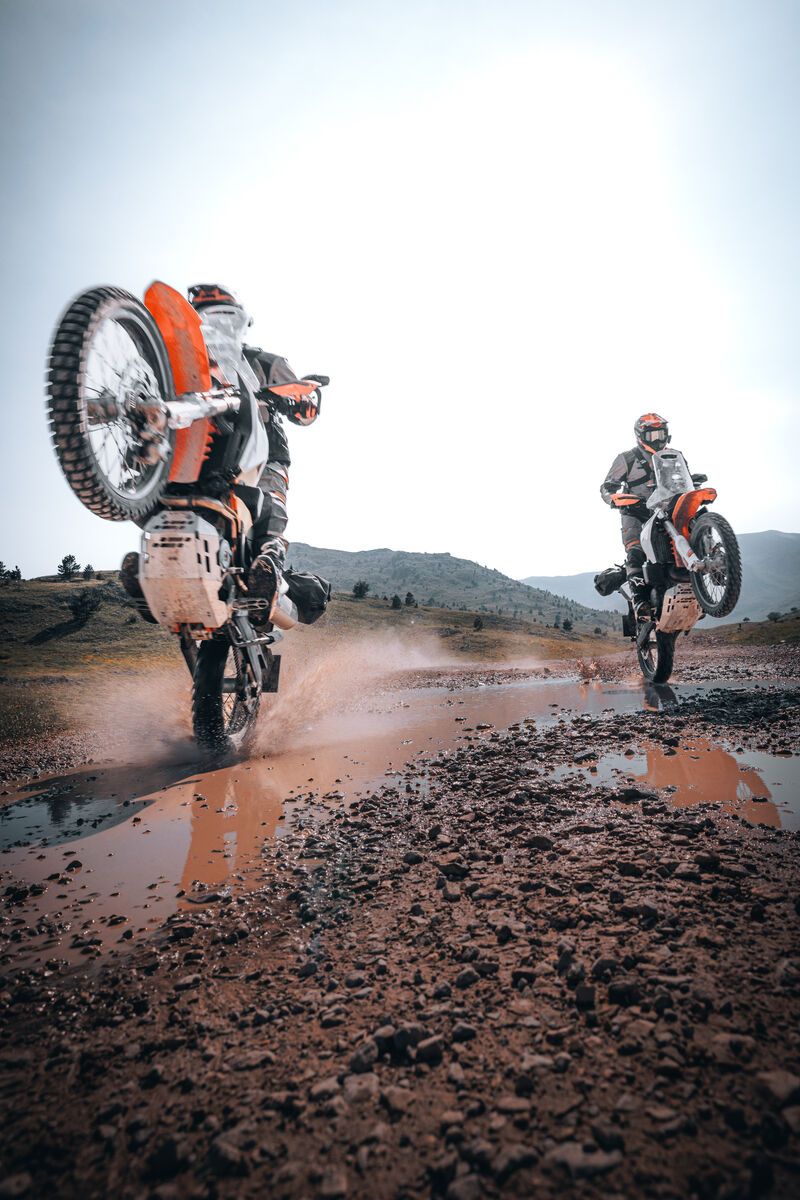 Two riders on adventure bikes splashing through a puddle on a mountain dirt road